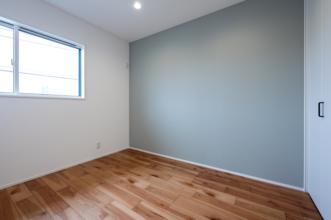 ナチュラルな木目の床とアクセントクロスが特徴の居室。柔らかな光が差し込み、落ち着いた雰囲気を演出しているシンプルな空間。