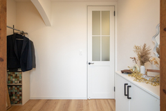 シンプルでスッキリとしたデザインの玄関ホール。ドアや壁の白色が空間を広く明るく見せ、ナチュラルな木目の床材が温かみを添える。