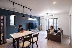 床にはヘリンボーン調のフローリング。リビングのクロスは白を基調としつつ、テレビ背面のみアクセントにネイビーを選択。雰囲気に合わせ、カーテンではなくブラインドを採用した。住宅街に位置するため、プライバシーにも配慮。隣家からの視線が気になる窓には、擦りガラスが選ばれている【ＩＤＫ 住まいの発見館】
