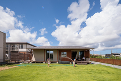 広々とした緑の庭で子供たちが遊んでいる様子。快晴の空の下、開放感溢れる魅力的なスペース。