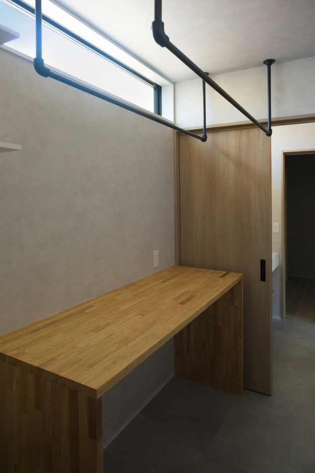 天井に設けられたパイプが便利なランドリールーム。ナチュラルな木製の作業台はアイロンがけやたたむ作業に最適。シンプルな設計が使いやすさを引き立てる。