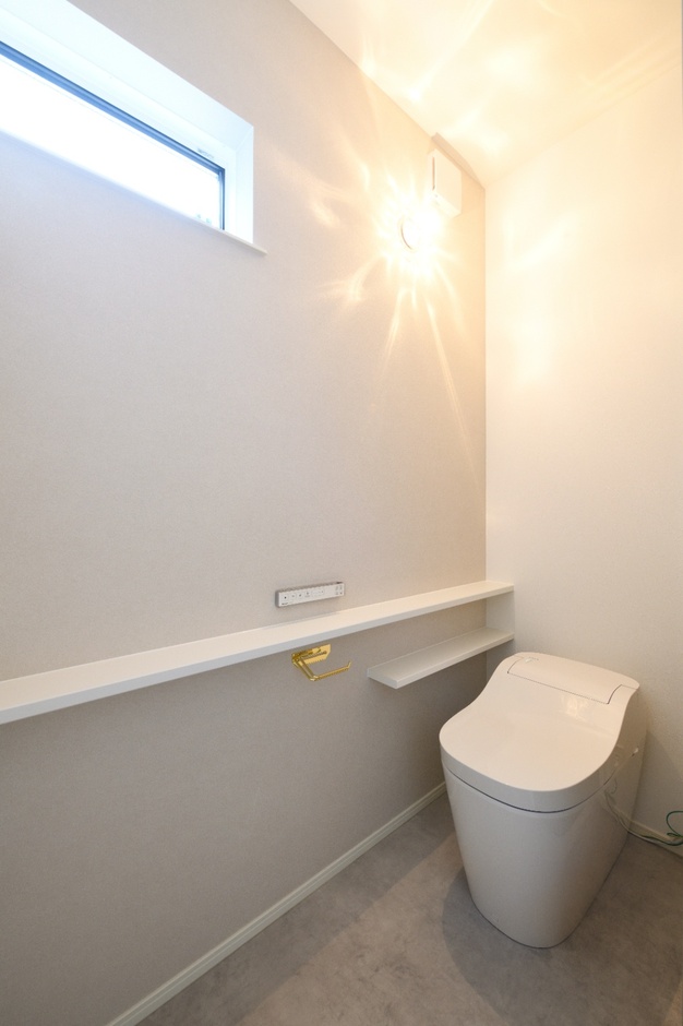 コンパクトながら機能的なトイレ空間。シンプルな照明と窓が、明るさと開放感を提供し、毎日の利用を快適にする。