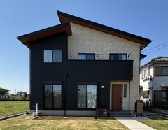 モダンなデザインの二階建て住宅の外観。コントラストのある壁材と大きな窓が特徴で、広がる庭も魅力的である。【サンアイホーム】
