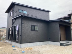 シンプルでモダンなデザインの二階建て住宅。落ち着いた色調の外壁が、周囲の景観に溶け込みながらも個性を放つ。【フラット】
