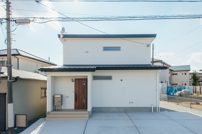 清潔感のある白い外壁を持つシンプルなデザインの住宅。落ち着いた雰囲気の木製ドアがアクセントとなり、スッキリとした印象を与えている。