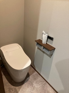 シンプルで機能的なデザインのトイレ空間。木目調の棚と落ち着いたカラーの床が、温かみのある雰囲気を演出している。【フラット】