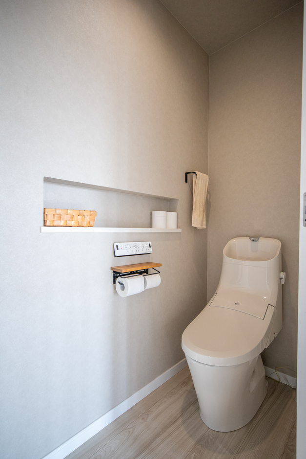 シンプルで機能的なトイレ空間。壁には便利な棚が設けられ、トイレットペーパーなどの収納に最適である。白を基調とした清潔感のあるデザイン。