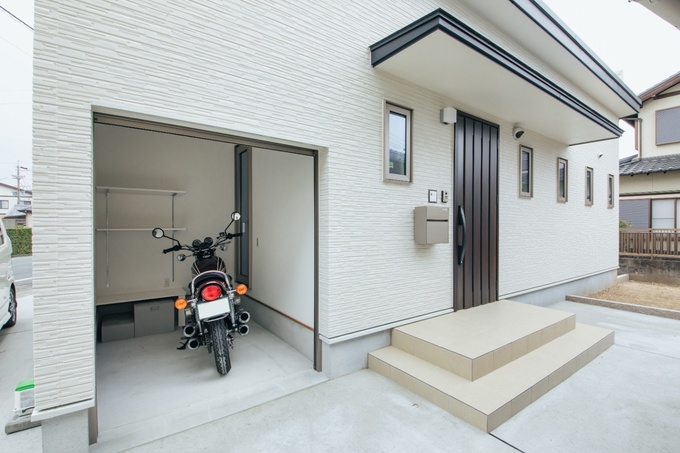 白い外壁に囲まれた洗練されたバイクガレージ。必要な収納スペースを確保しつつ、バイクの出し入れが容易で、機能的なデザインが魅力的。