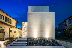 夜間にライトアップされたモダンな外観の住宅。直線的なデザインが特徴で、周囲の住宅と比べて洗練された印象を与える。【iDpluss アイディープラス】