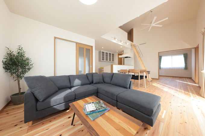 明るく広々としたLDK。大きなL字型ソファとダイニングセットが配置され、家族が集まって過ごしやすい空間。高い天井と木の温もりを感じるフローリングが特徴的。