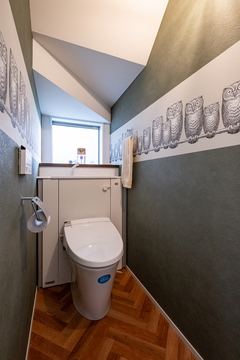 ふくろう柄の輸入クロスがかわいいトイレは階段下スペースを活用。タンク部分を収納に隠し、スッキリさせた【金子工務店/めぐみ不動産】