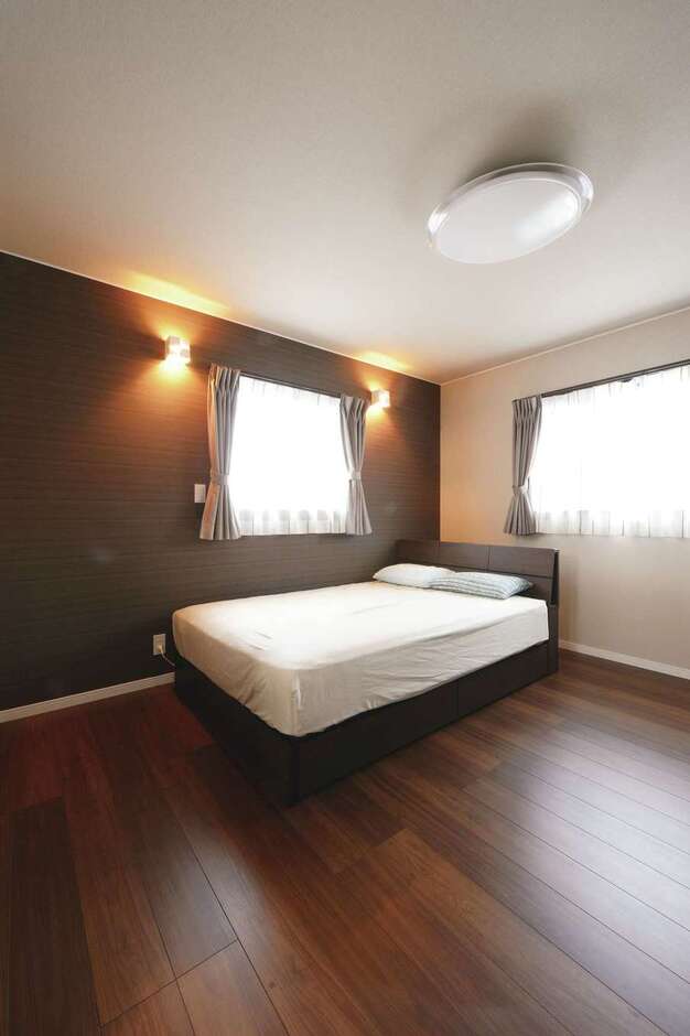 1階のLDKと変化をつけるため、ダークブラウンの床を採用した主寝室。アクセントクロスを照らす間接照明がリラックス効果を高めてくれる