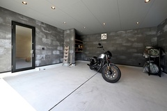モダンなデザインのインナーガレージ。広々としたスペースにより多様なバイクの収納や整備が可能である。コンクリートの壁がクールな印象を与える。