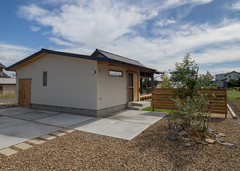 のどかな住環境にしっとり馴染んだ平屋づくりの外観。塗り壁とガルバリウムの使い分けにより、素材の良さがいっそう引き立てられた。ヘリンボーン柄に施工した外部収納の木製扉も、上品なアクセントを添えている