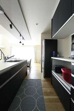 下がり天井でアクセントを付けたキッチンスペース。対面キッチンとダイニングテーブルを並べて一直線に配置し、配膳や片付けの動線を短縮。キッチンの奥にはパントリーも設けている