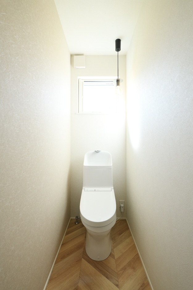 シンプルで清潔感のあるトイレ空間。木目模様の床が温かみを与え、コンパクトながら機能的にデザインされた空間である。