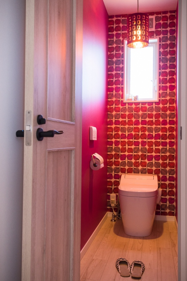 鮮やかな赤色のアクセントクロスが印象的なトイレ空間。小窓から自然光が差し込み、明るく清潔感のある雰囲気を演出している。