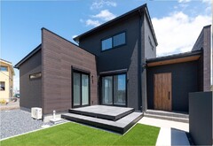 モダンなデザインの二階建て住宅の外観。シンプルな濃色の外壁と木材が組み合わさり、高級感と落ち着きを持つ仕上がり。【三交不動産】