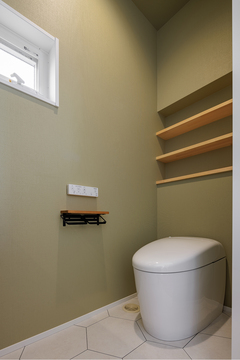 シンプルで清潔感のあるトイレ。緑色の壁紙と木製の棚が落ち着いた空間を演出している