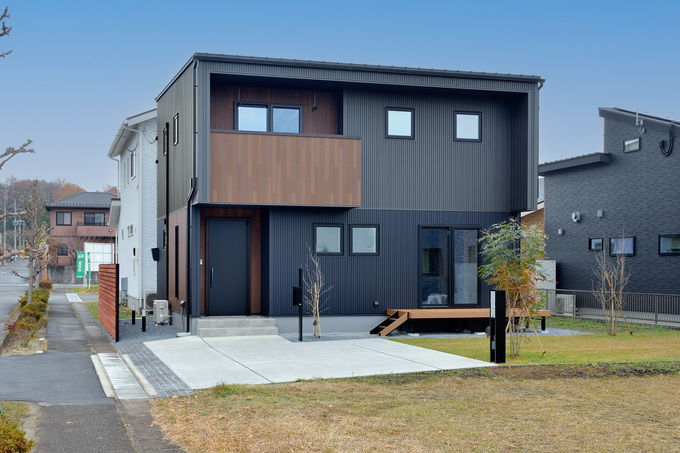 シンプルなデザインの二階建て住宅の外観。黒とブラウンを基調とした配色がシックでスタイリッシュな印象を与える。ガルバリウム金属・木目サイディングで暖かみと彩りをもたらす。