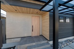 落ち着いた濃色サイディングと軒から壁へと繋がる木目が印象的なエントランス。街並みに溶け込みながらも存在感を放つシンプルモダンな佇まい。【アッシュホーム】