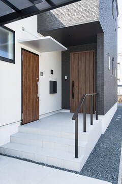 二つの木製ドアがアクセントのモダンな玄関外観。質感の異なる壁面が洗練された印象を与える。分離型の二世帯住宅。【トキワハウス デザイン アンド ビルド（常盤工業）】