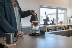 大きな窓が開放感をもたらすキッチン。シンプルなデザインで、作業スペースが広く居心地が良い。コーヒーを楽しむための落ち着いた空間になっている。【コスモ建設】