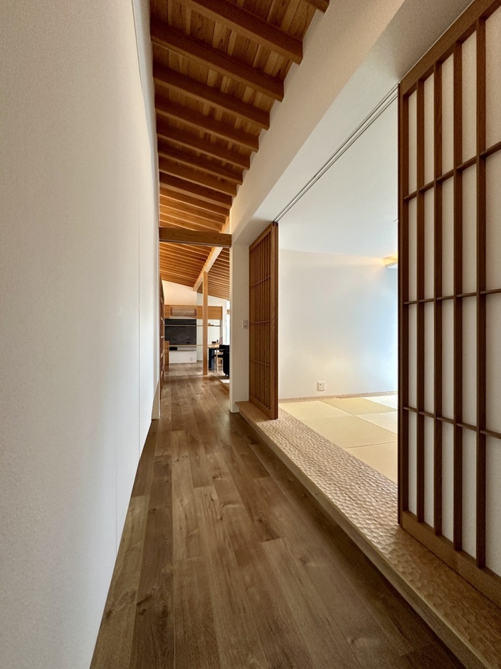 縦格子の引込戸を開け、建具の存在を消した様子。ホールからリビングへと続く勾配天井の規則正しく並ぶ垂木が美しい。