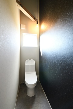 シンプルながらモダンなデザインのトイレ。暗色の壁と白い便器がスタイリッシュなコントラストを生む【REIWA HOUSE（令和ハウス）】