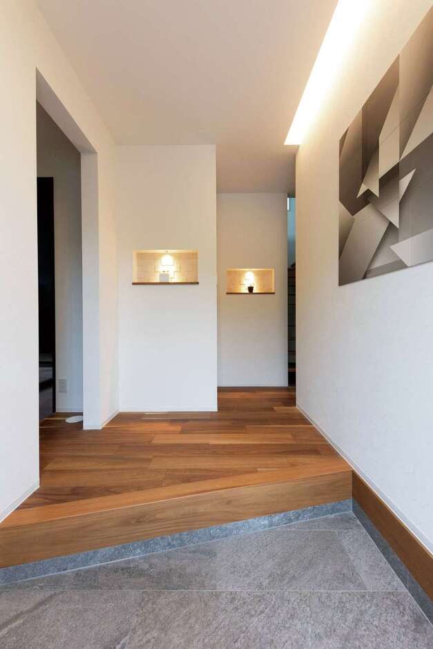 玄関を入った正面に照明付きニッチを2つ設置して視覚的なポイントに。右側のアーティスティックな壁掛けは、調湿・脱臭機能を持ったエコカラット製