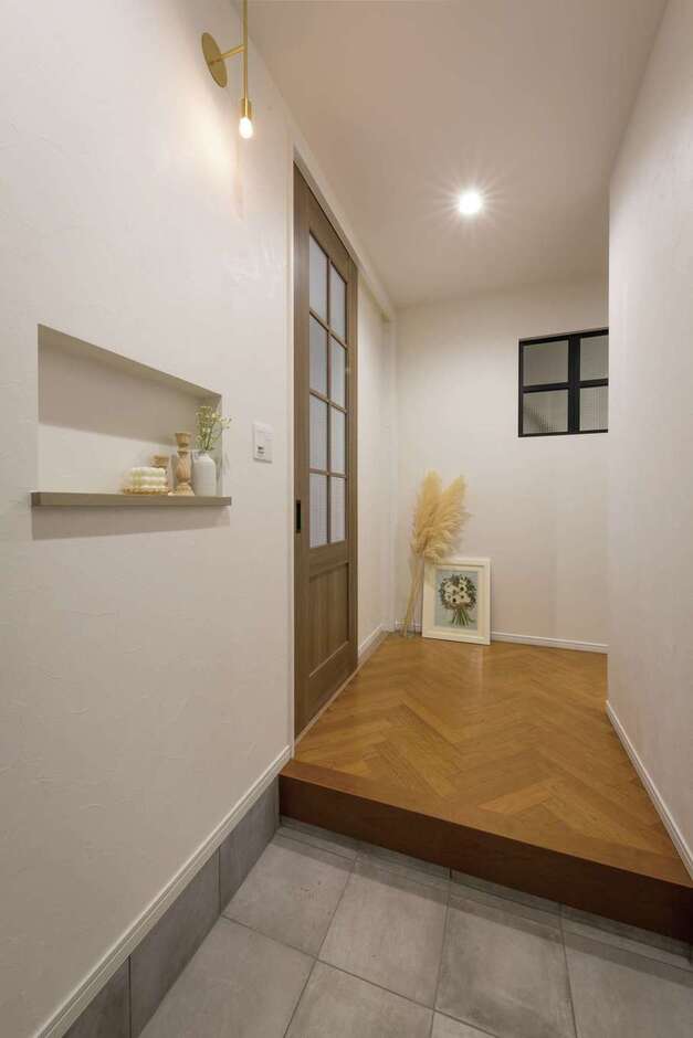 ヘリンボーン張りのフロアタイルを張った玄関ホール。マットな質感がすてきなリビングドア、繊細なデザインがおしゃれな照明、造作ニッチのバランスが絶妙