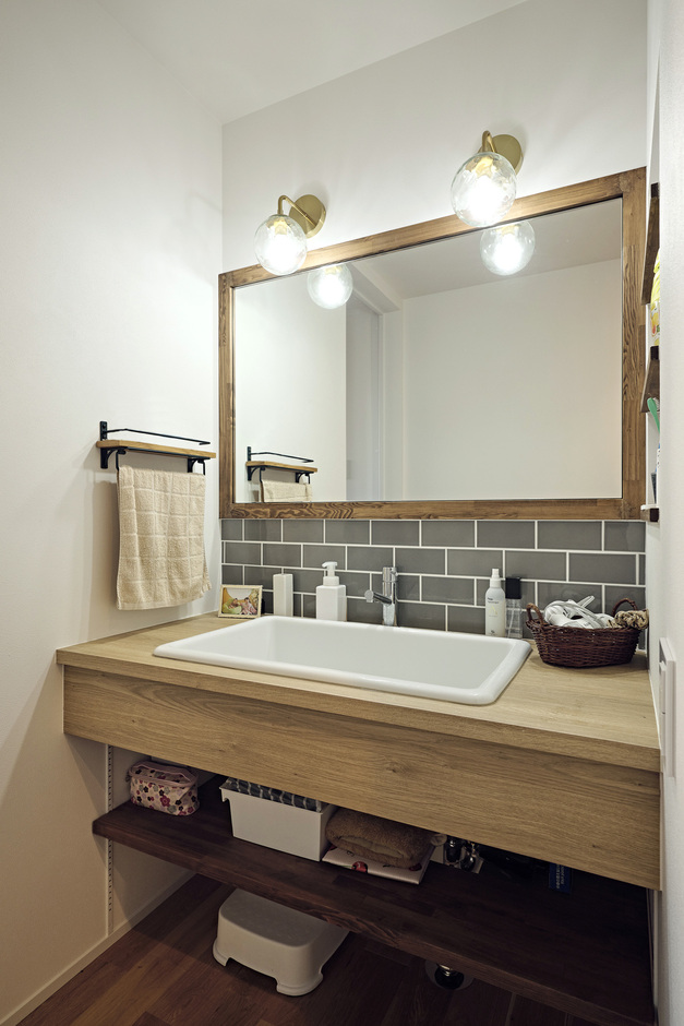 木製の造作の洗面台に合わせて、木製の枠付きの鏡を採用。幅を広くして、二人でも使えるようにした。奥行きの深い実験シンクを採用し、スロップシンク代わりに子どもの上履きを洗ったり、手洗いをしたりするのに使うこともできる