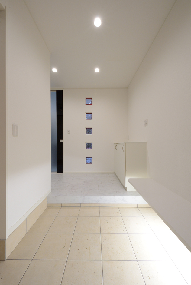 北側の玄関は、暗くならないよう色の入ったガラスブロックで明かりをとる。白で塗装した木のベンチは、ブーツや足袋を履くときに便利