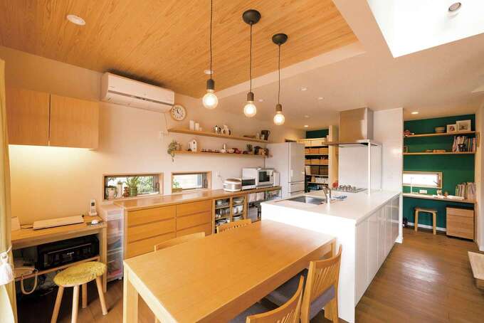 夫妻のセンスと暮らしぶりが伝わってくるDK。天井の杉板とワークスペースのクロスが、空間の役割を穏やかに分割する。左手の作業机は造作で、来客時にはダイニングテーブルにつけて使えるよう高さがそろえられている