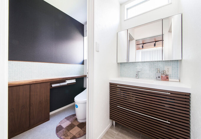 洗面室とトイレにあしらったガラスタイルが爽やかな水回り。トイレの収納はネットで見つけたお気に入りを大工さんにアレンジしてもらい設置。ラメ入りの黒いクロスがおしゃれ