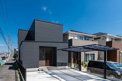 モダンなデザインの2階建て住宅。シックなブラックの外壁とスタイリッシュなカーポートが街並みに調和している。【サンジョーホーム】