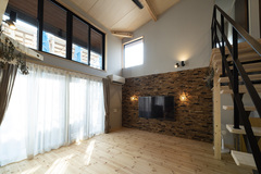 大きな窓から自然光がたっぷり差し込むリビング。壁面の石造りのデザインと吹き抜けが贅沢な空間を演出。