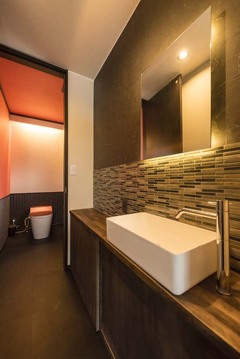 モダンなタイル使いとの洗面台。トイレの天井にはアクセントカラーのオレンジのクロスを用いた【アトリエサクラ】