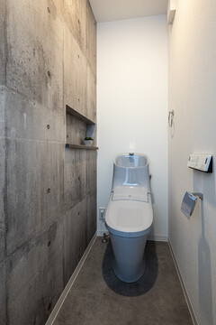 スタイリッシュで落ち着いたデザインのトイレ空間。コンクリート風の壁がアクセントとなっている。【トキワハウス デザイン アンド ビルド（常盤工業）】