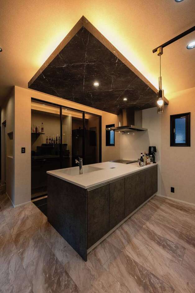 下がり天井と間接照明がおしゃれなキッチン。黒い半透明の引き戸で冷蔵庫や棚を隠し、生活感を排除