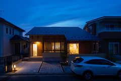 夜の家の外観。温かい光が漏れ出し、周囲と調和した静かな住宅街の一角。