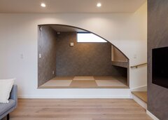 リビングの一角に設けた小上がりの和室。垂れ壁をアーチ形状に切り取って、モダンな空間に。子どもたちが遊んでいる様子がキッチンから目が届くので安心。ゲストが泊まりに来たときは、ロールカーテンで仕切ることもできる【nattoku住宅】