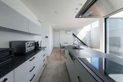 ショールームに足を運んで採用したkitchenhouseのキッチンと、正面の窓に広がる開けた視界が、忙しい家事の時間も心を軽くする。生活感を抑えるため、冷蔵庫は背中側に配したパントリー内に設置。キッチン部分に敷かれたタイルはパティオへと続き、広さを演出【MABUCHI】