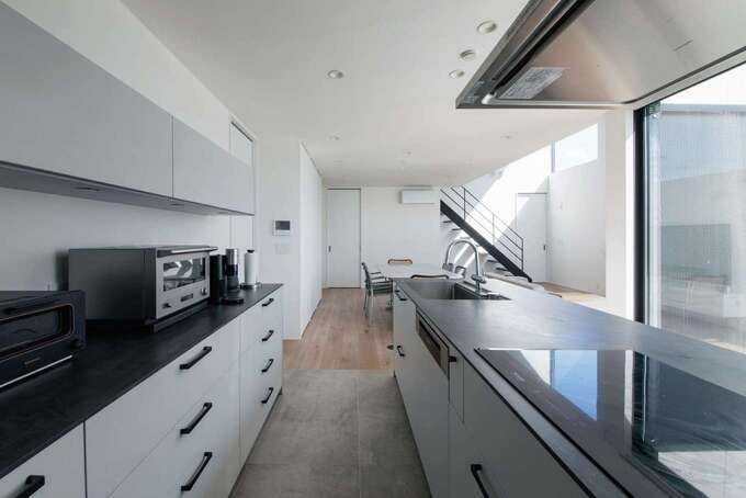 ショールームに足を運んで採用したkitchenhouseのキッチンと、正面の窓に広がる開けた視界が、忙しい家事の時間も心を軽くする。生活感を抑えるため、冷蔵庫は背中側に配したパントリー内に設置。キッチン部分に敷かれたタイルはパティオへと続き、広さを演出