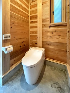 ウッド素材で温かみのあるトイレ空間。自然光が差し込む窓があり、心地よい雰囲気が漂う。外からのトイレなので土間使用。【明城】