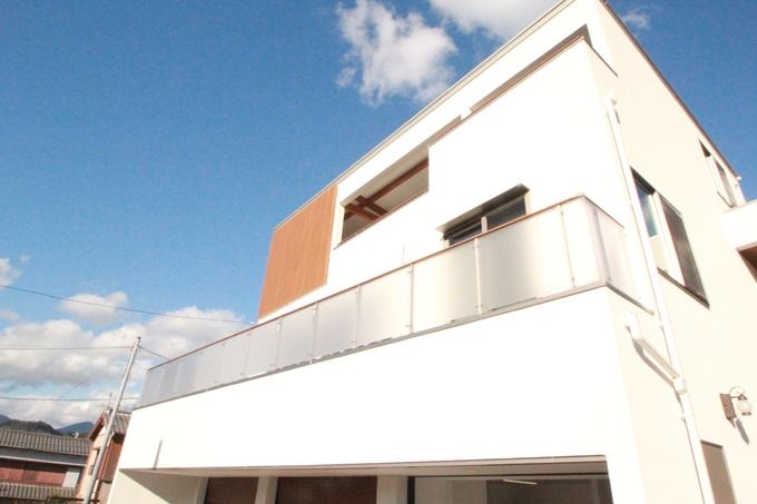 モダンなデザインの3階建て住宅。上階バルコニーの一部に設置された木製フェンスが、白い外壁のアクセントになっています。