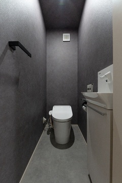 ダークトーンで統一されたシンプルなトイレ空間。壁や床がシックな色調で、落ち着いた雰囲気が漂う。機能性重視のデザイン設定で快適さを提供。【ユースタイルハウス　上村建設】