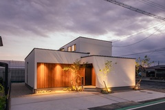モダンで洗練された住宅の外観。ナチュラルな木材とシンプルな白い壁のコントラストが美しく、夜間にはライトアップされて雰囲気が際立つ設計である。