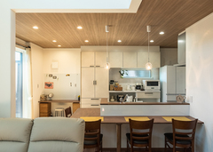 ダイニングテーブル一体型の対面キッチン。木目調の下がり天井がニュアンスを与える。キッチンの背面は、食器棚、調理家電、冷蔵庫まですべて白で統一した。壁のRの出隅は標準仕様で、安全性を保ちつつ優しさを表現している