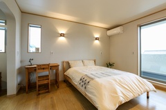 木製の家具が温かみを感じさせる、モダンでシンプルな寝室。壁掛けライトが落ち着いた雰囲気を演出している。【ビビットホーム（アクティス）】